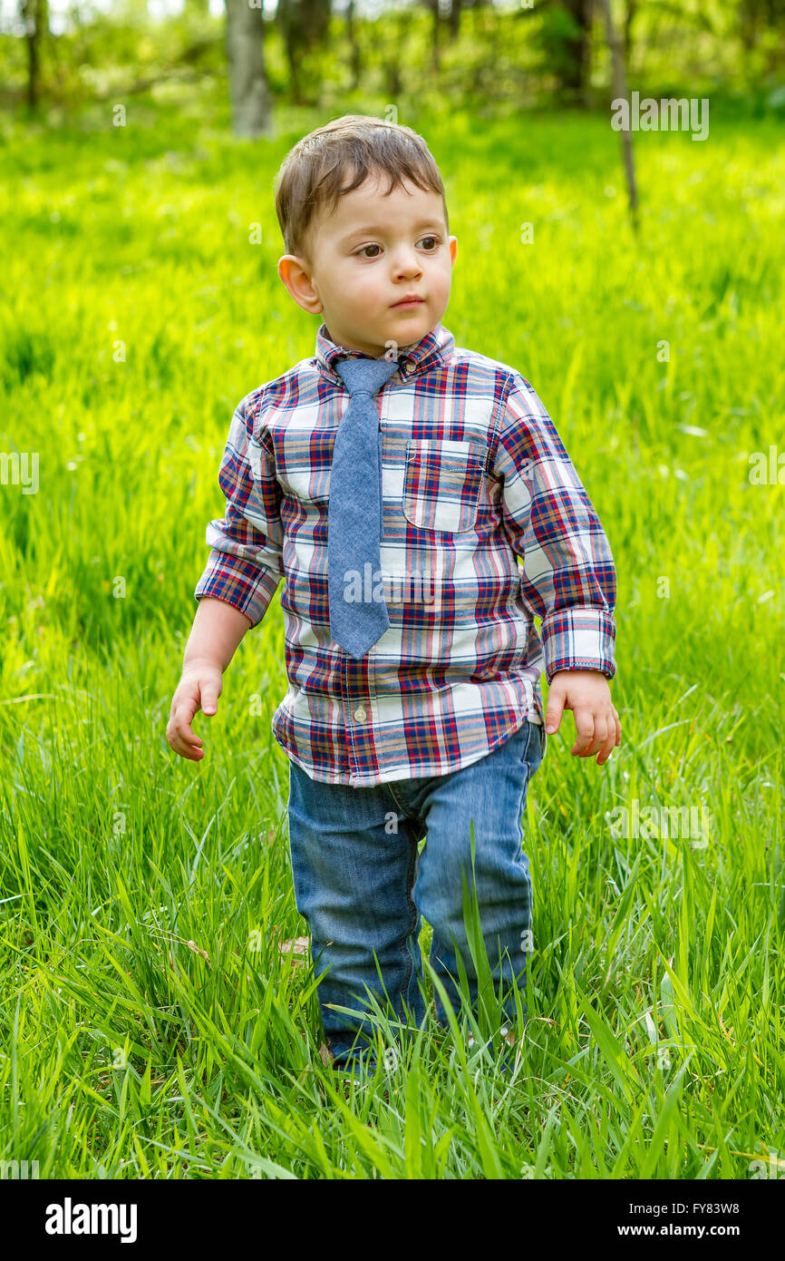 Little boy in the blue shirt jeans and striped tie walking in the grass in park Stock Photo