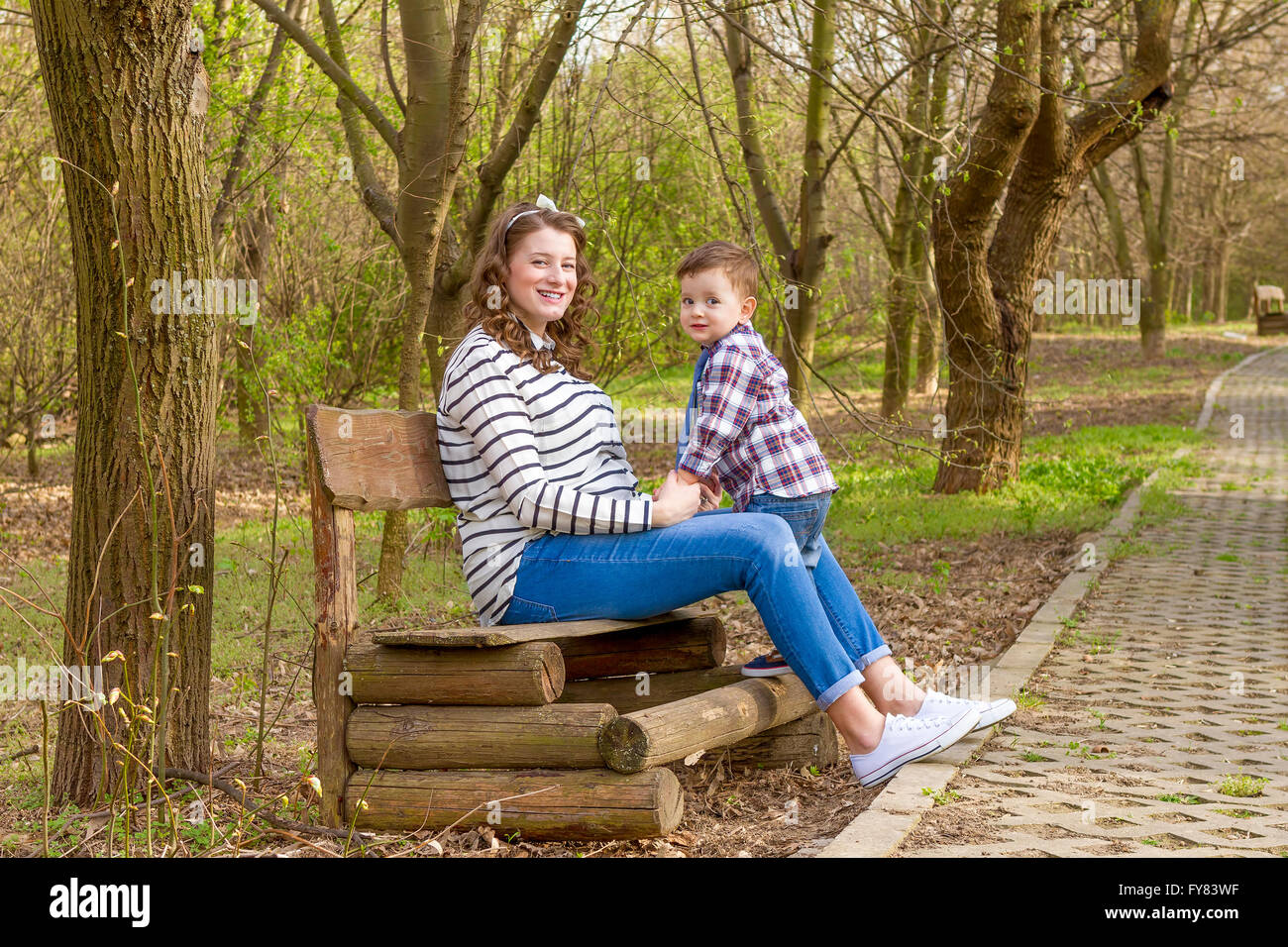 Beautiful pregnant woman outdoor with her little boy in the park on bench. Stock Photo