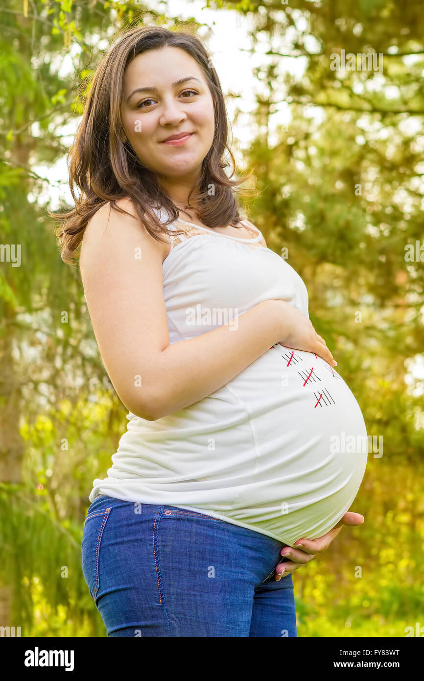 Portrait of smiling pregnant young woman outdoors in warm summer day. Stock Photo