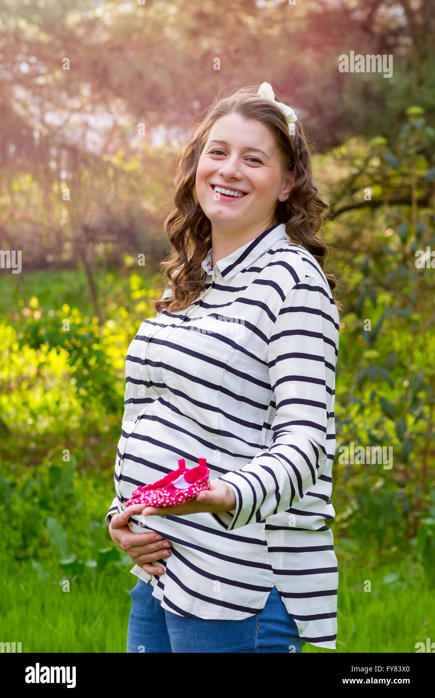 Close up of a pregnant woman holding baby shoes in her hands in a park Stock Photo
