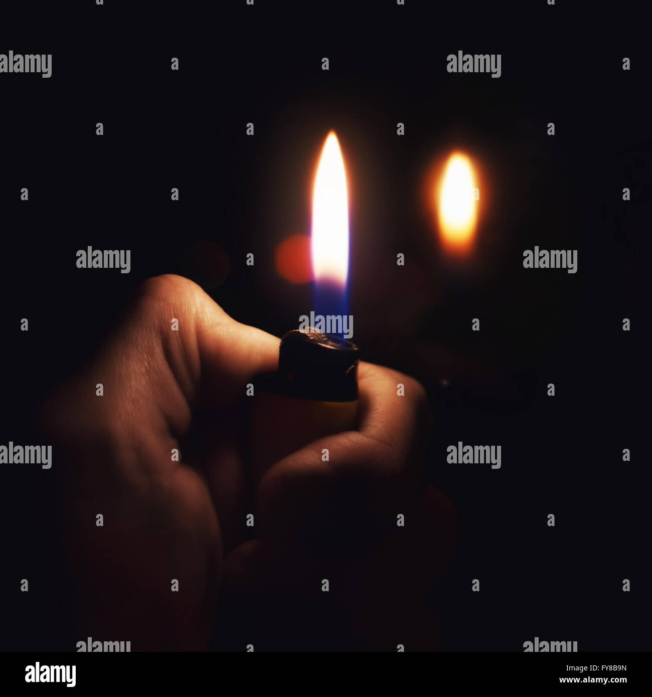 Male hand holding a burning lighter in the dark Stock Photo