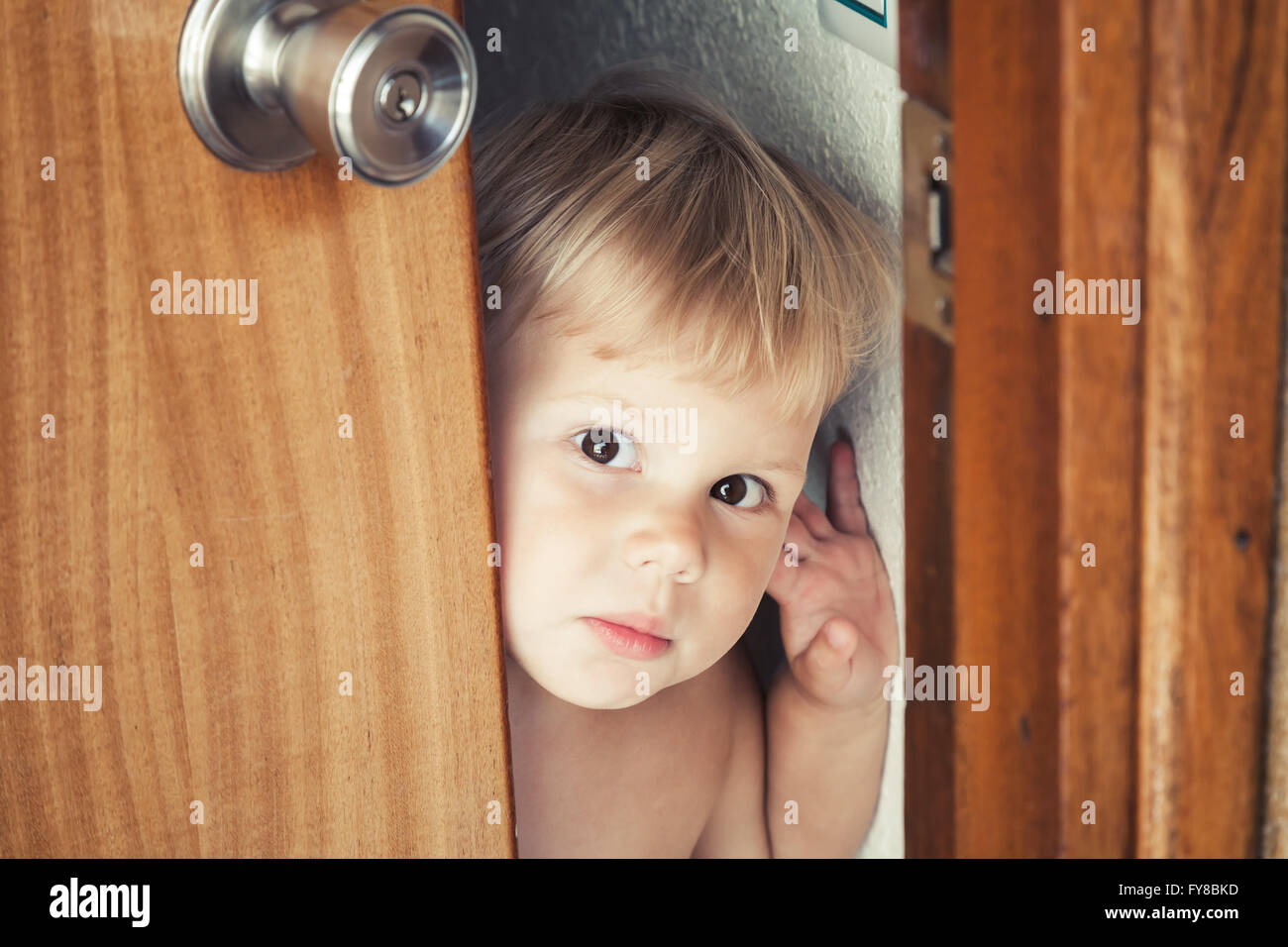 Little Caucasian blond baby opens door and looks outside Stock Photo