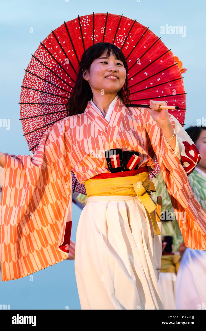 Yosakoi hinokuni dance festival, smiling woman in yukata jacket, dancing with red parasol over her shoulder, early evening, at Kumamoto, Japan. Stock Photo