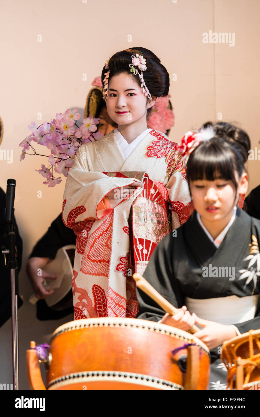 Japanese stage show for springtime and cherry blossom. Teenage girl sitting drumming in foreground with geisha in kimono dancing behind. Stock Photo