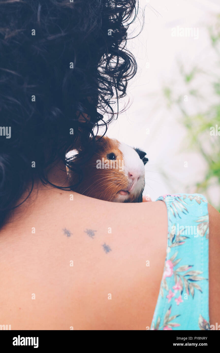 Back view of young woman with Guinea pig on her shoulder Stock Photo