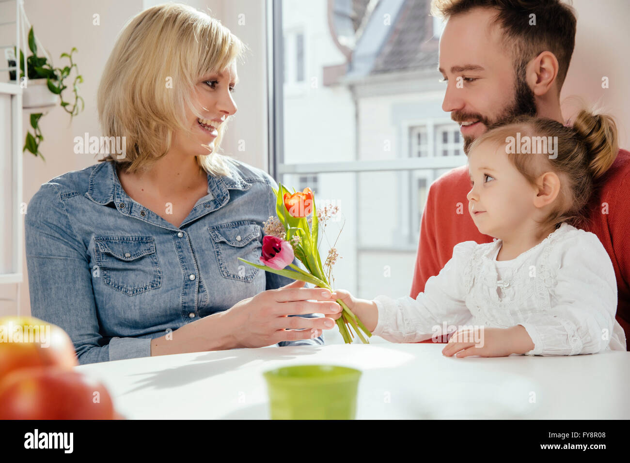 Little girl giving her mother flowers while father is watching Stock Photo