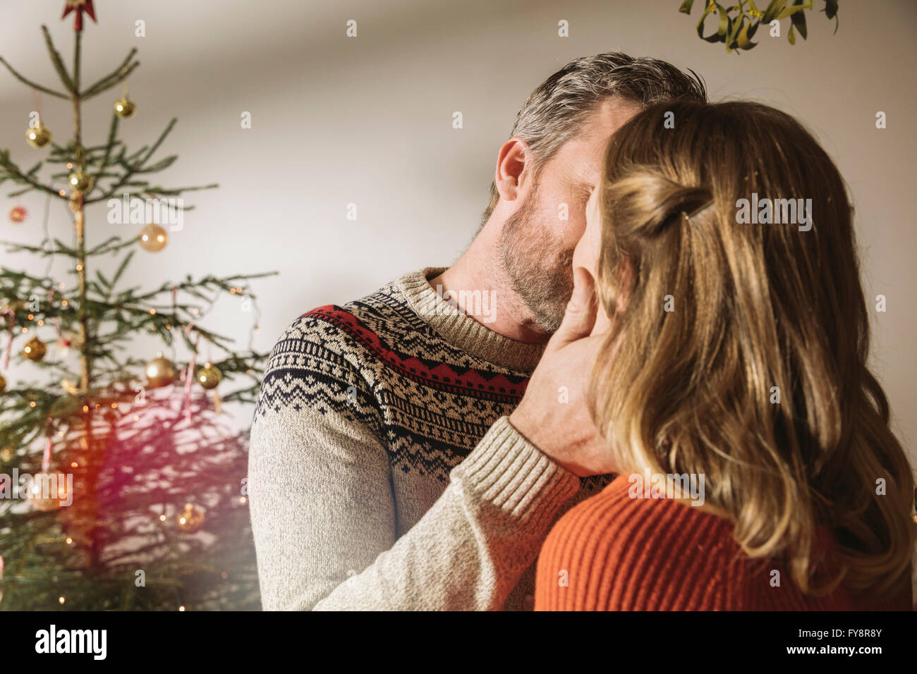 Happy couple standing in front of Christmas tree, kissing under ...
