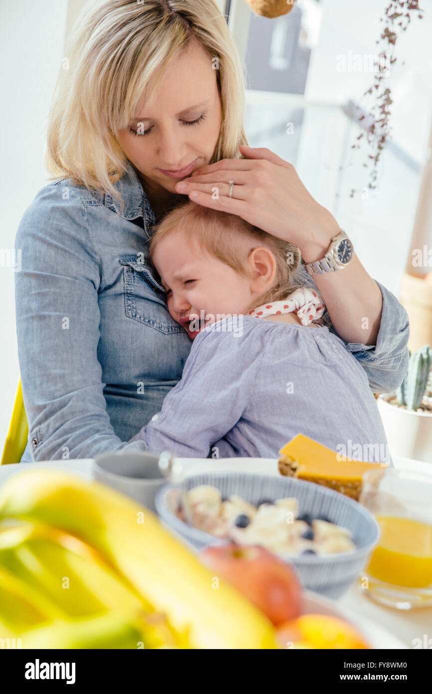 Little girl crying in mother's arms at breakfast table Stock Photo - Alamy