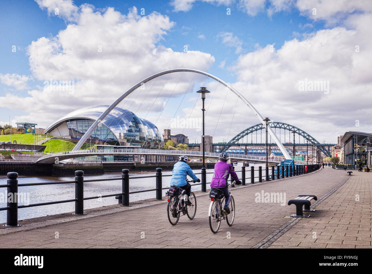 Cyclists riding along Newcastle Quays, with a view of the Tyne Bridges, including the Millennium Bridge, the Tyne Bridge, and al Stock Photo