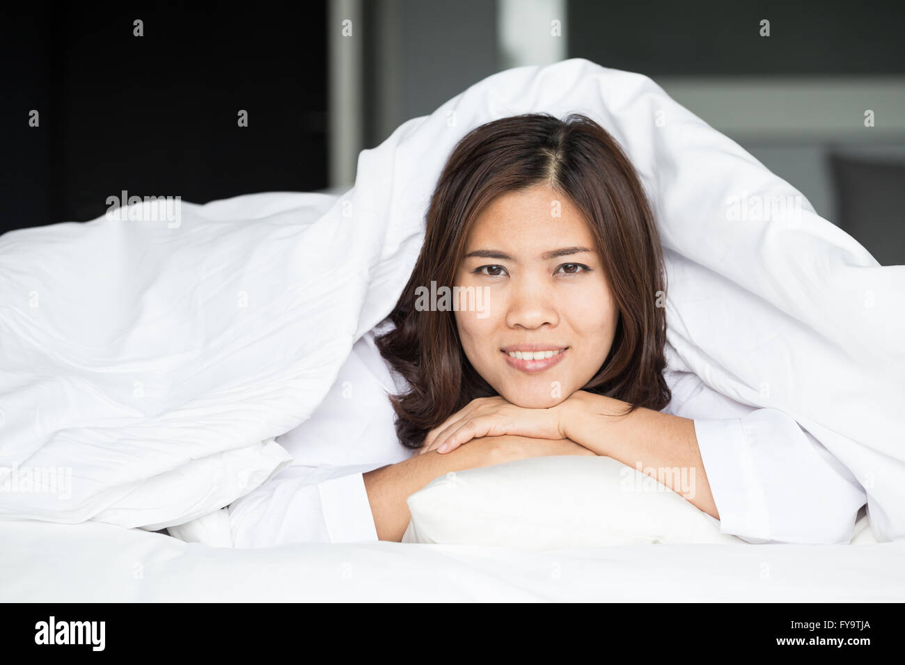 Asian Woman Lying At The End Of The Bed Underneath The Quilt And