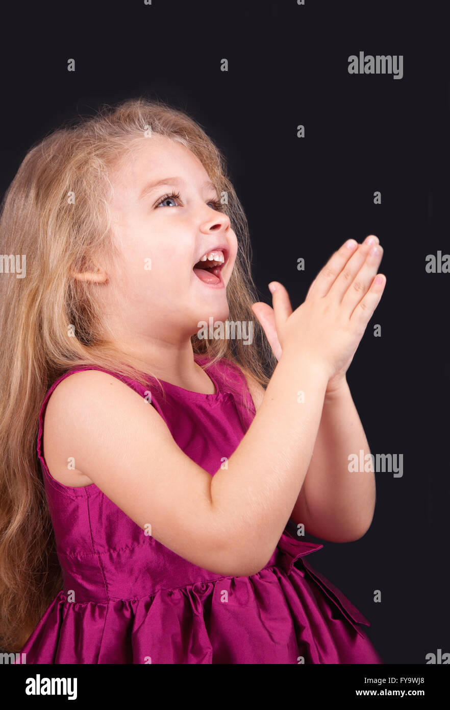 Little cute girl in a pink dress on a black background in the studio ...