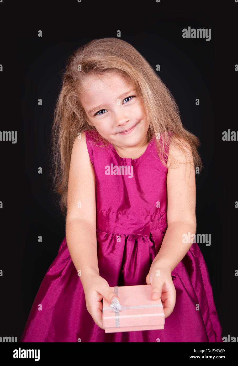 Portrait of a joyful little girl in a pink dress with a gift in her ...