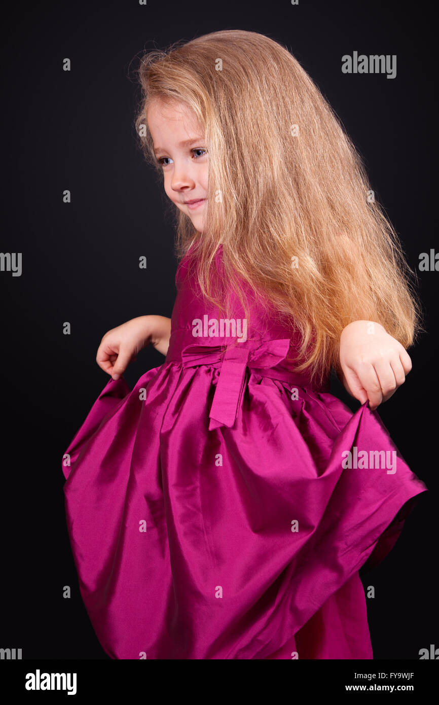 Studio portrait of a pretty little girl in a pink dress on a black ...