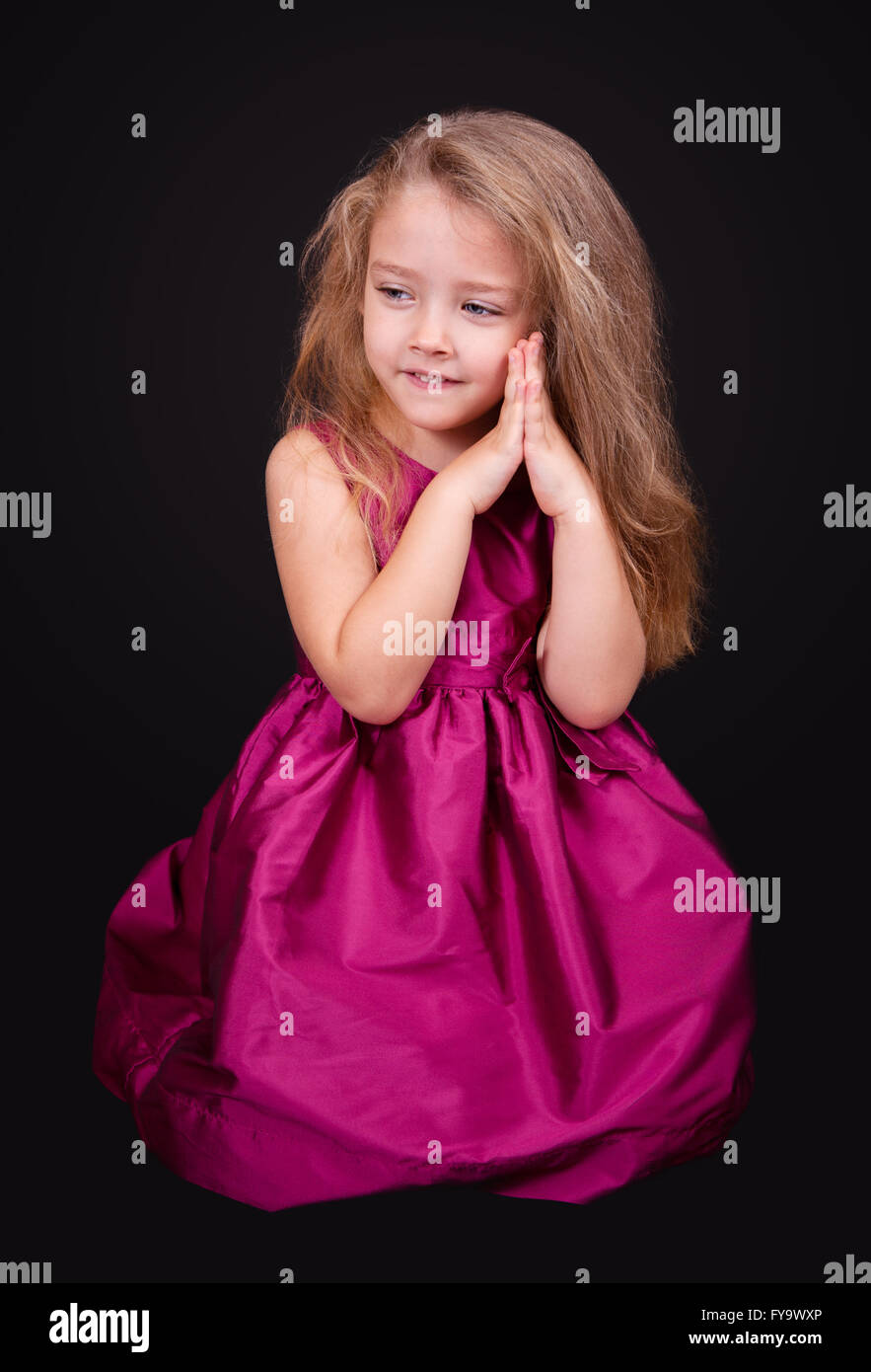 Little cute girl sitting on the floor in a pink dress on a black ...