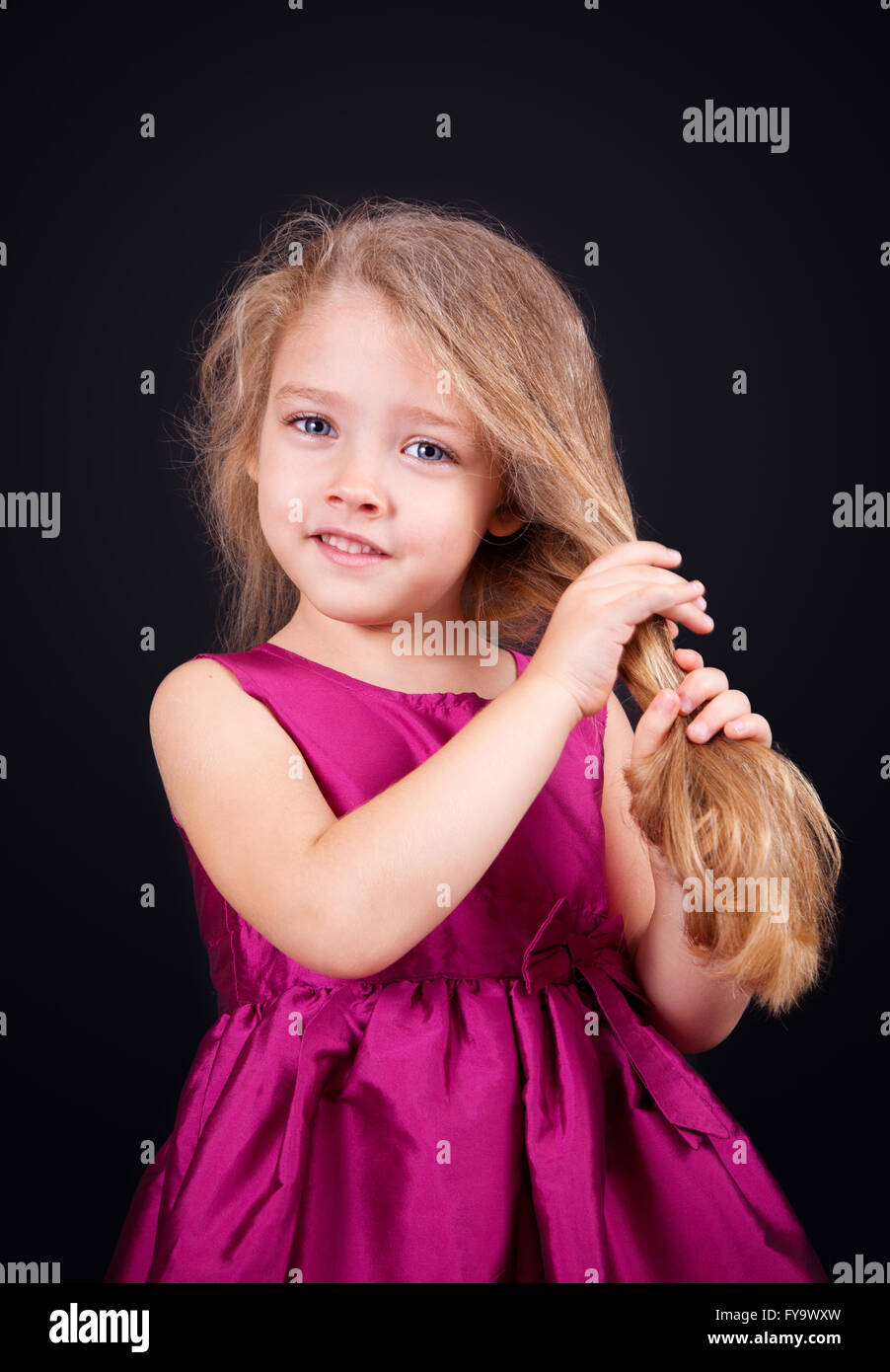 Little cute girl in a pink dress on a black background in the studio ...