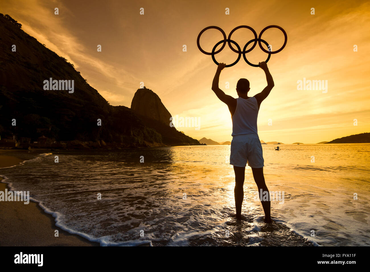 RIO DE JANEIRO - APRIL 2, 2016: Silhouette of an athlete holds Olympic rings at a sunrise scene in front of Sugarloaf Mountain. Stock Photo