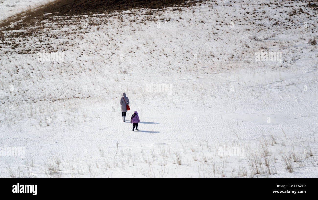 Woman and young child far away in the distance walking across a snow covered field Stock Photo