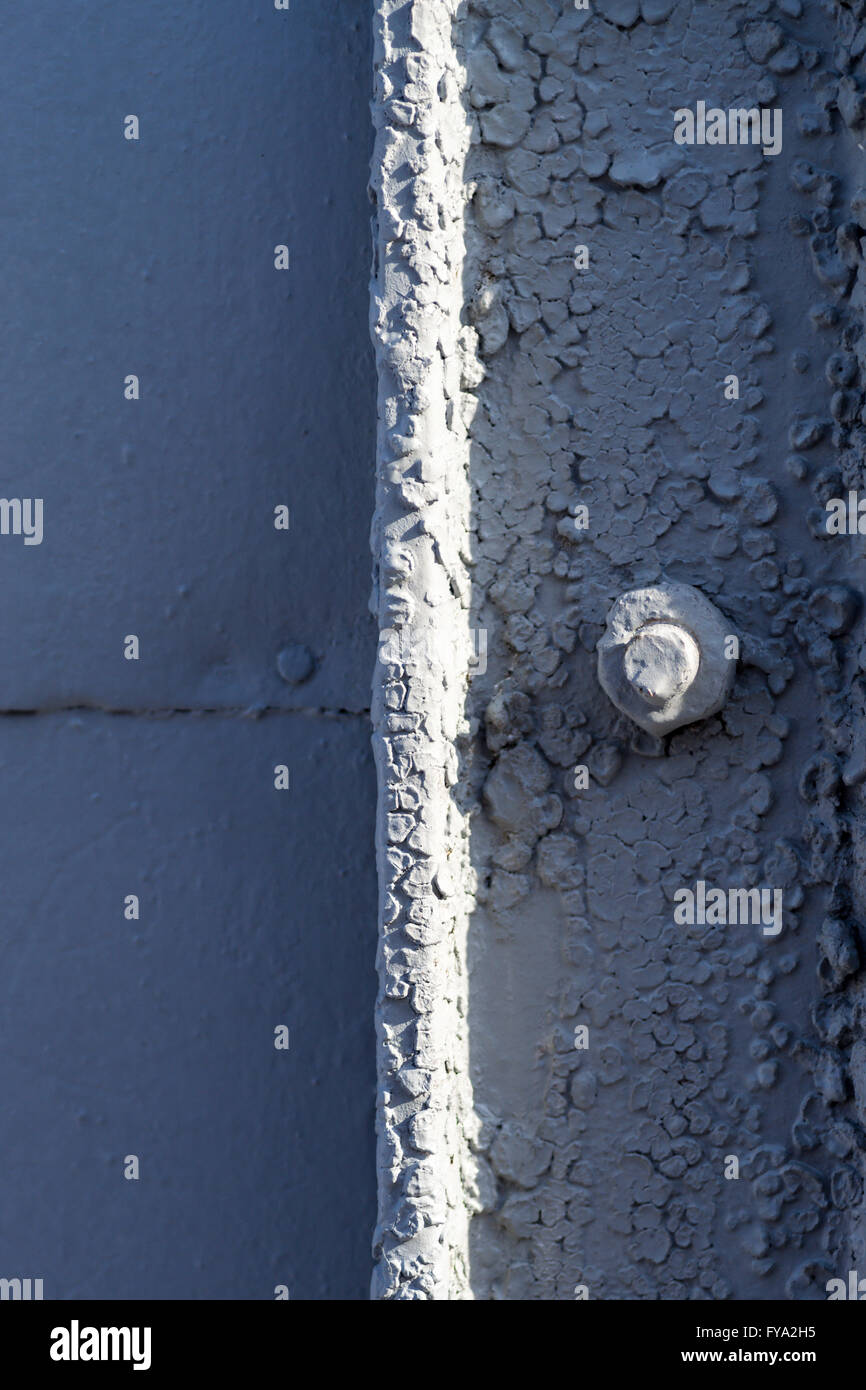 Closeup image of an old grey painted bolt securing a metal background