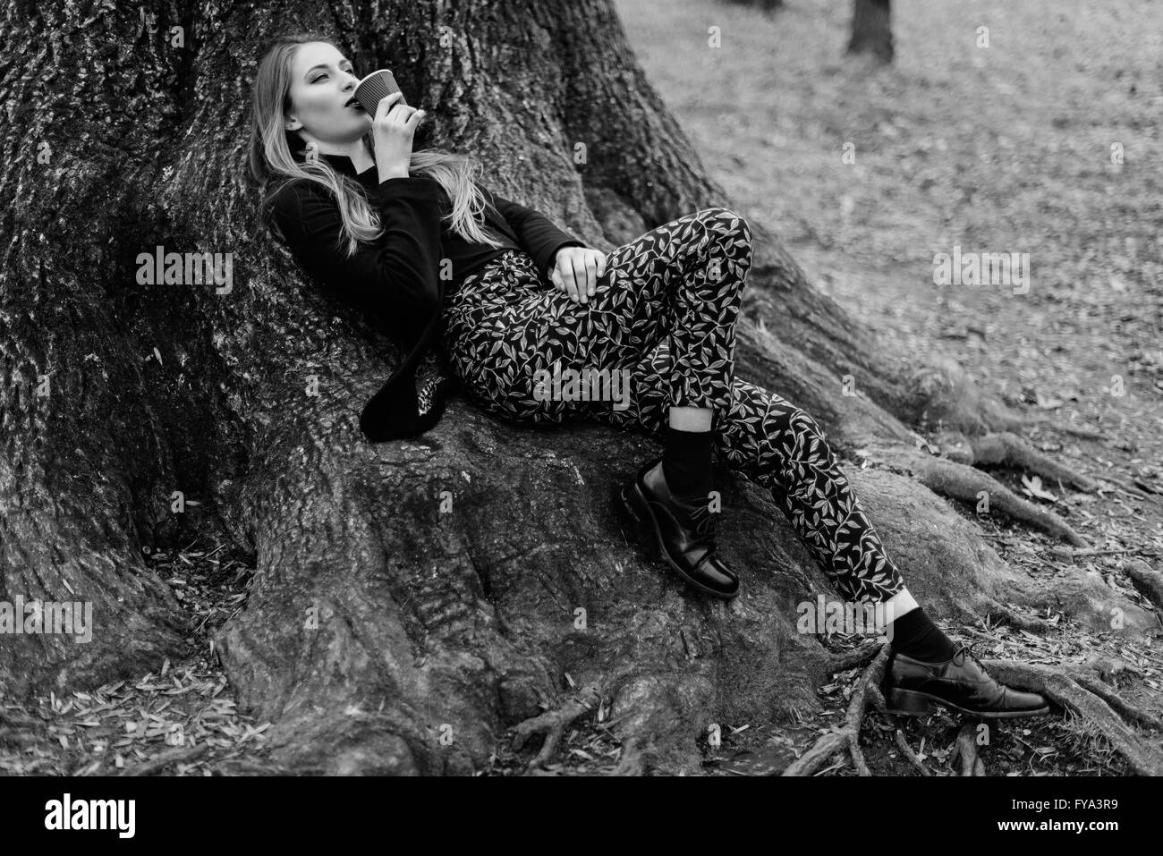Stylish young girl lying on the tree roots in spring park. Black and white Stock Photo