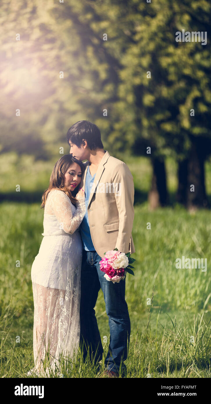 Expecting mom and dad, with flowers, holding each other in open grassy