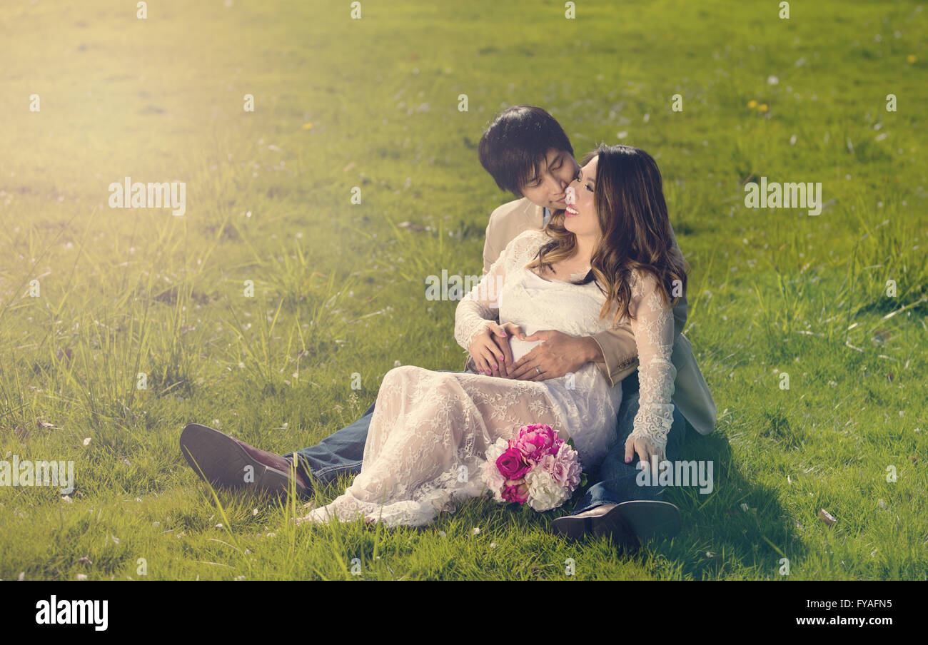 Expecting mom and dad lying in tall grassy field holding each other. Stock Photo