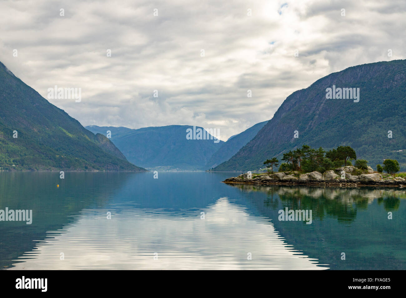 Small rocky and pine island at norwegian fjord with mountains on background Stock Photo