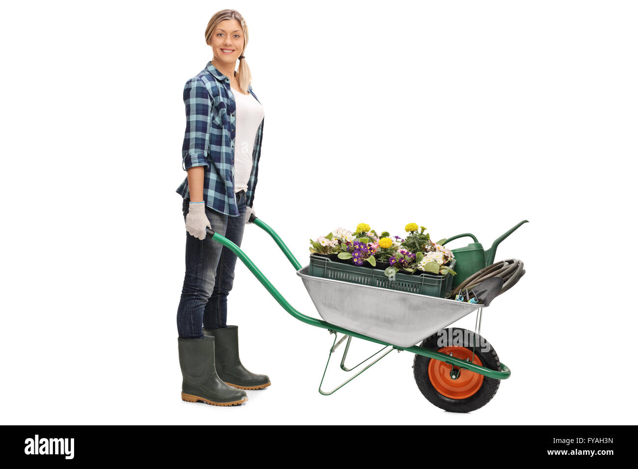 Full length portrait of a female gardener pushing a wheelbarrow full of gardening equipment isolated on white background Stock Photo