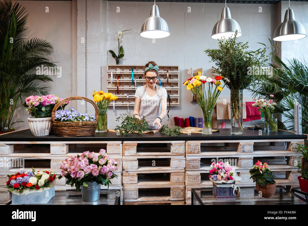 Smiling attractive young woman florist standing and working in flower shop Stock Photo