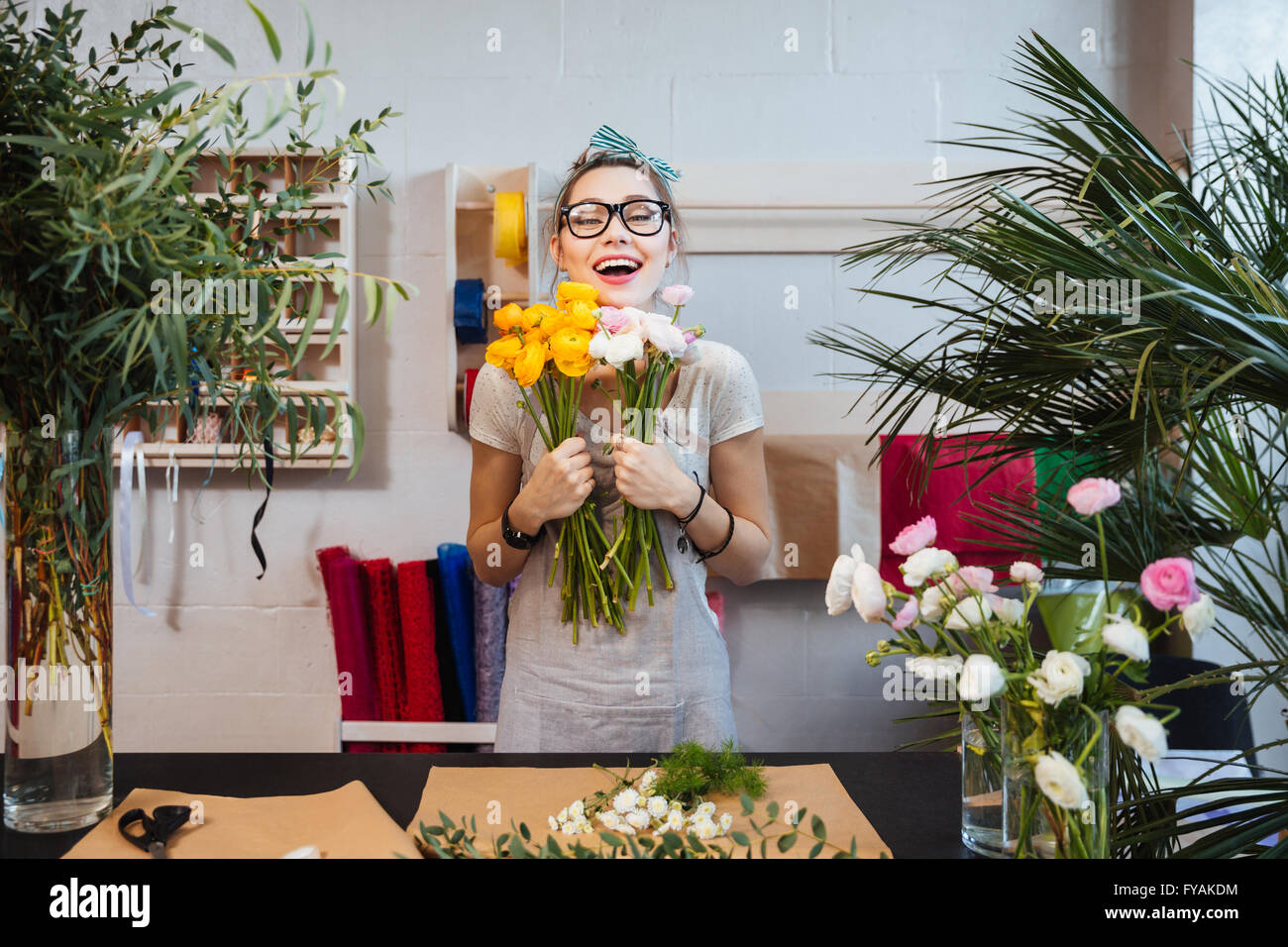 Happy excited young woman florist with bunch of flowers standing and laughing in shop Stock Photo