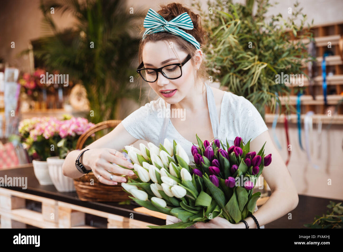 Cute lovely young woman florist in glasses taking care of tulips in flower shop Stock Photo