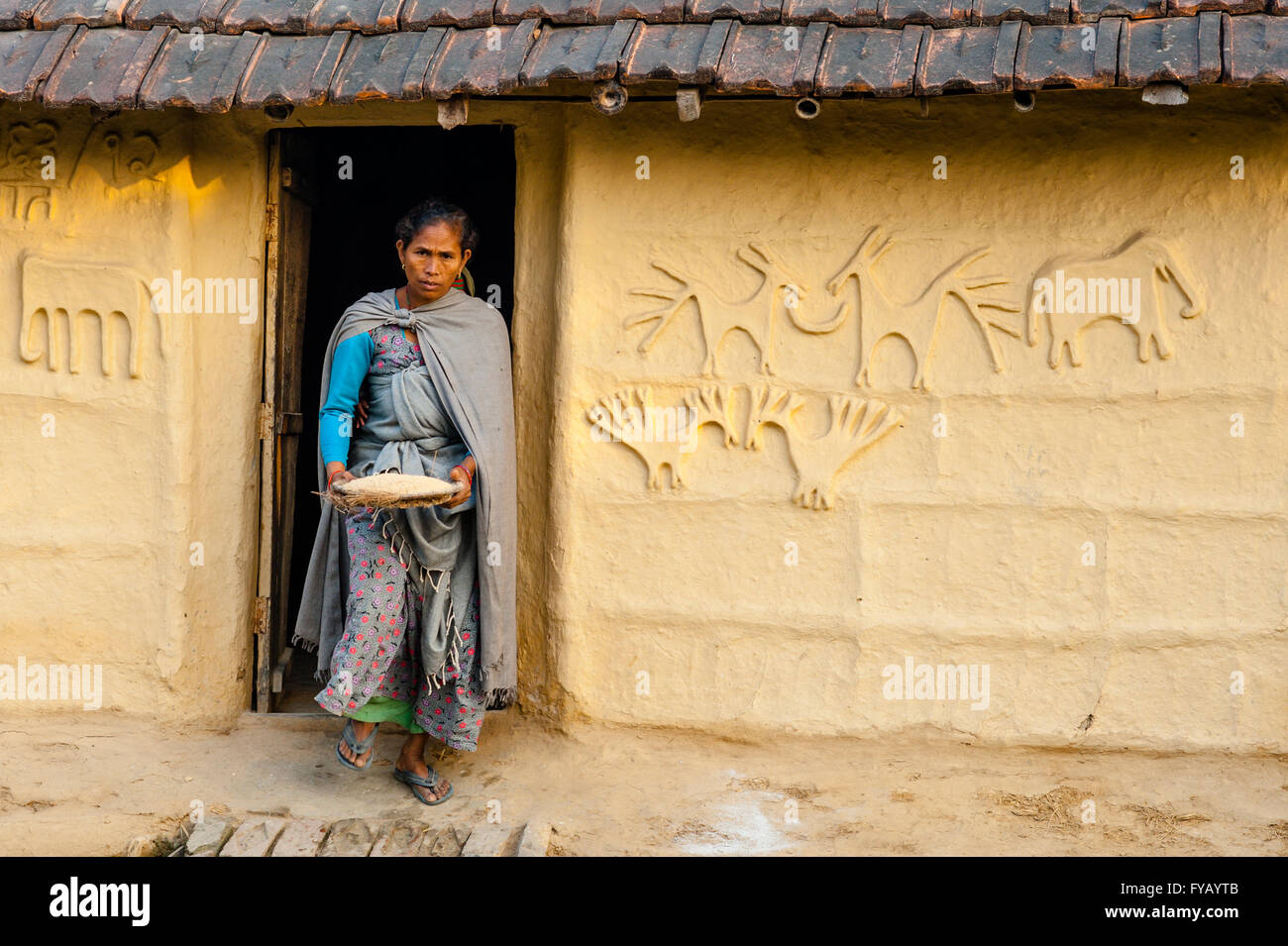 Tharu woman carrying rice exits through doorway of a traditional and decorated Terai rammed-earth home Stock Photo