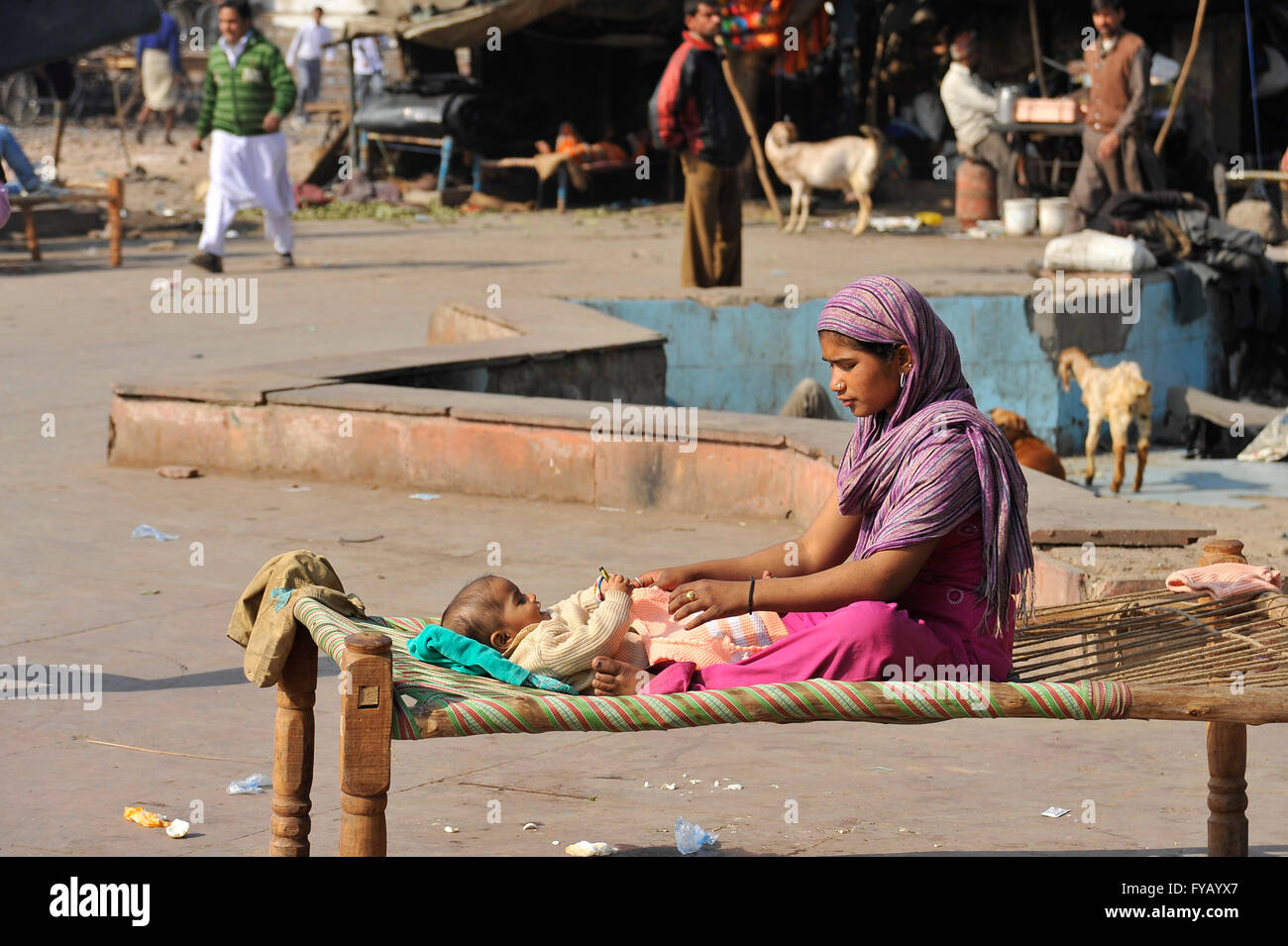 A young mother sits with her baby on a charpoy outside a shanty town in Old Delhi Stock Photo