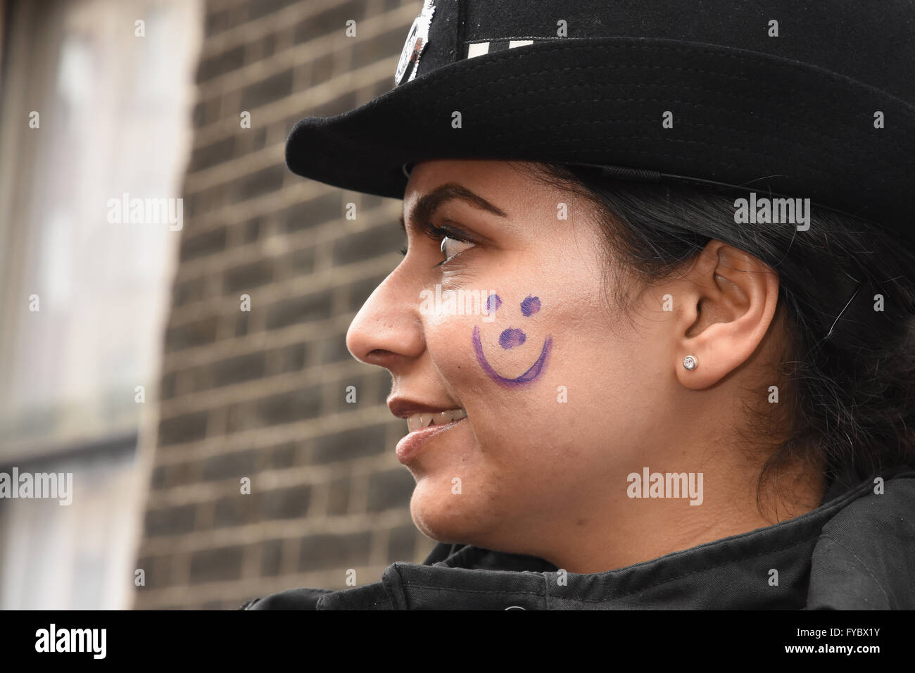Smiling Female Community Liaison Police Officer,with smiley face painting,Anti Austerity March,Gower Street,London UK Stock Photo
