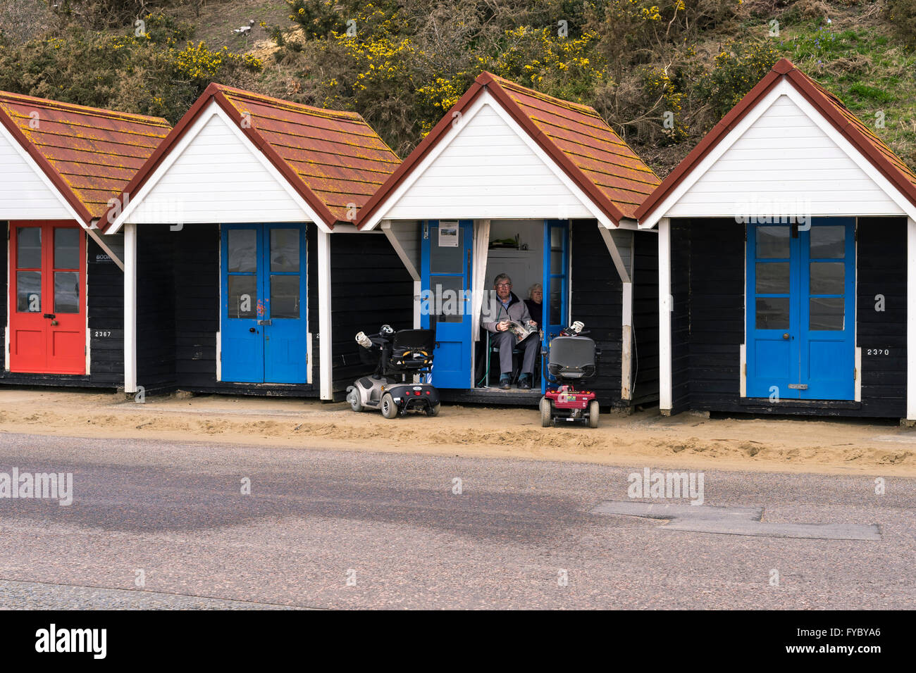 Elderly couple sit inside a public hire beach hut with pair of mobility scooters parked outside , Bournemouth, Dorset Stock Photo