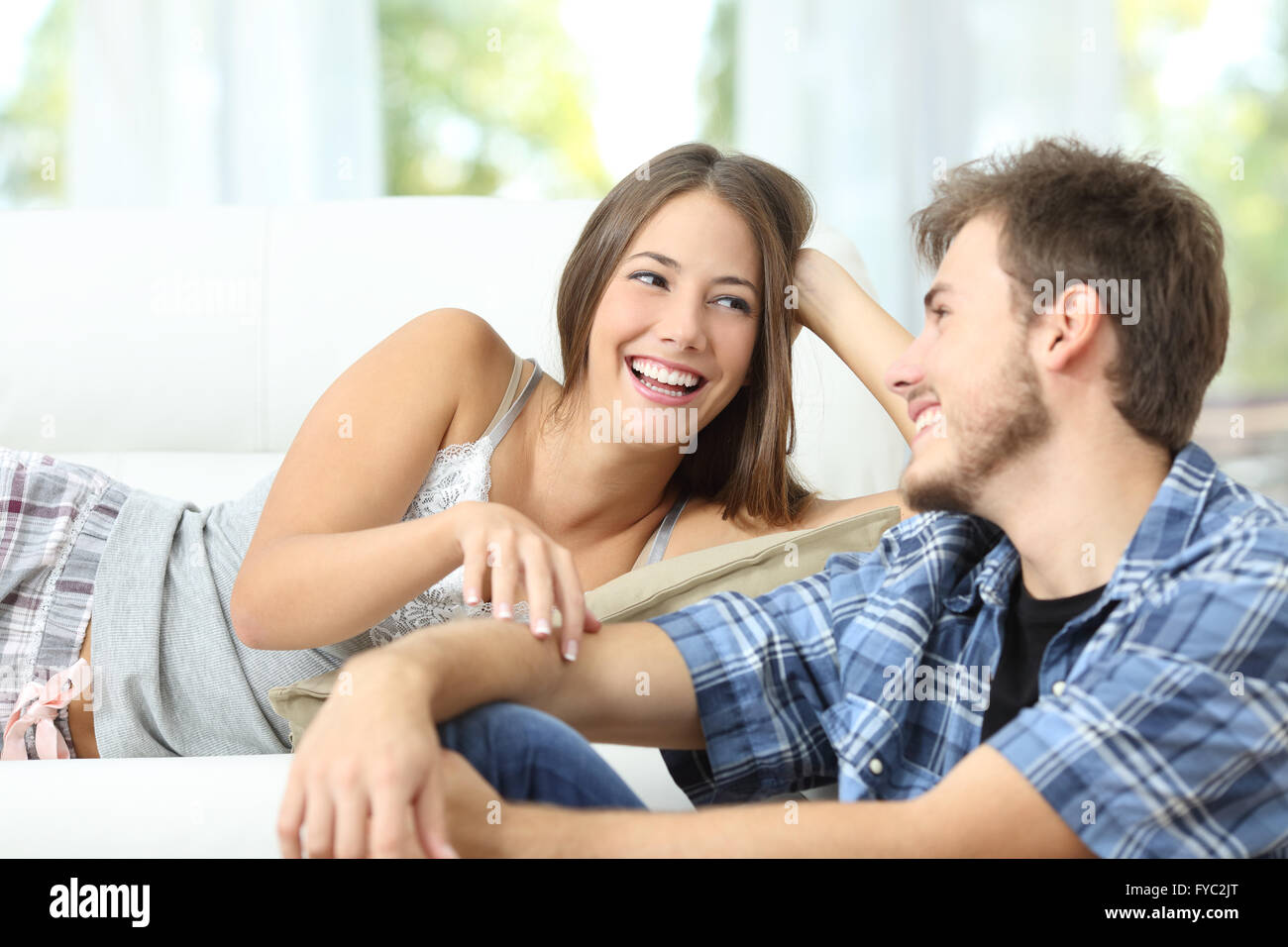 Happy marriage or couple flirting and laughing lying on a couch at home Stock Photo