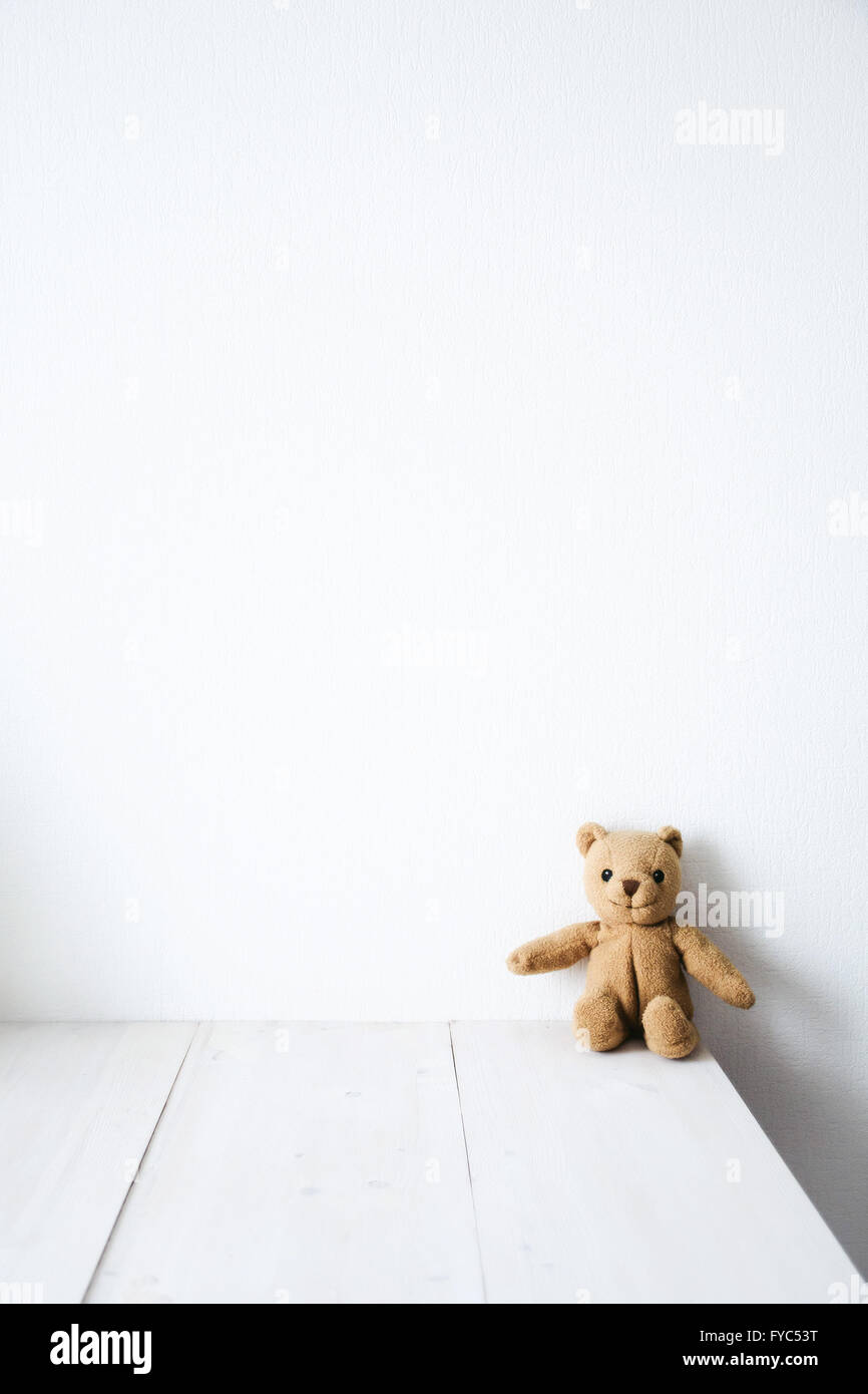Cute teddy bear sitting on white wooden table near white wall. Moody background Stock Photo