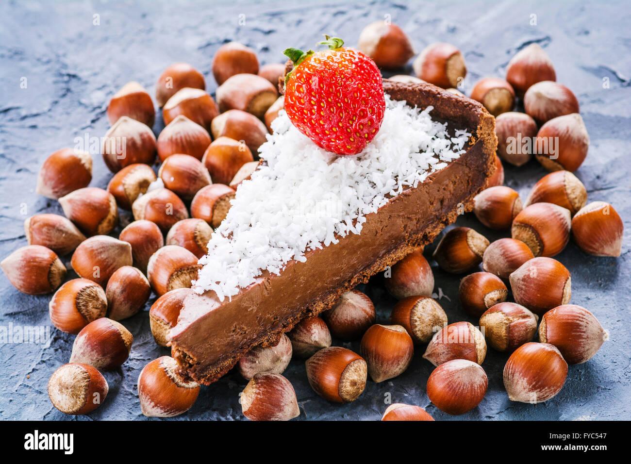 Slice of chocolate hazelnut mousse tart / chocolate pie decorated with coconut flakes and strawberry. Selective focus Stock Photo