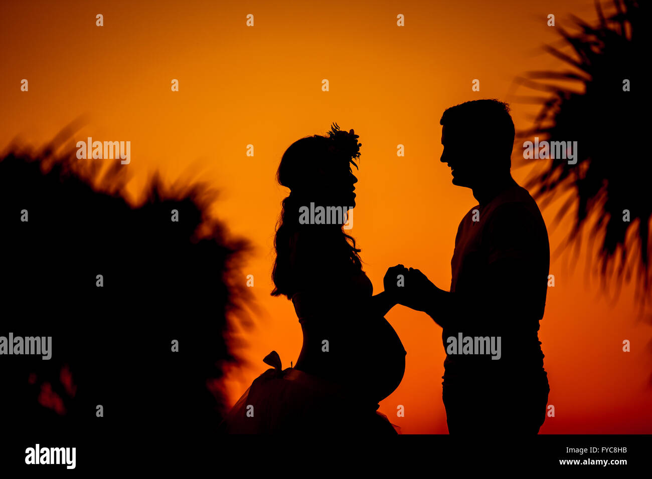 Silhouette of young couple expecting baby holding hands during orange ...
