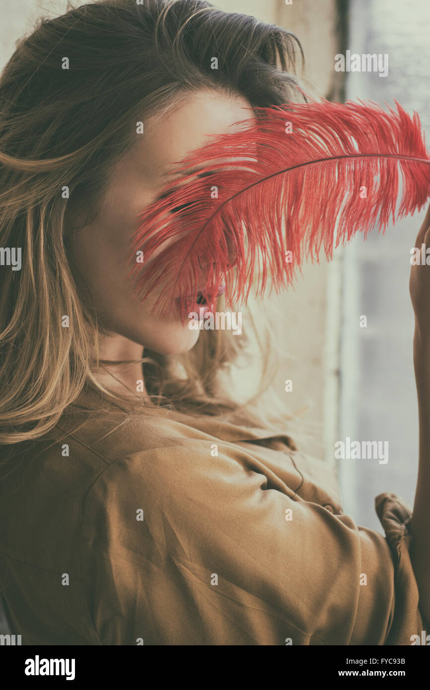 Young woman hiding face with a red feather Stock Photo
