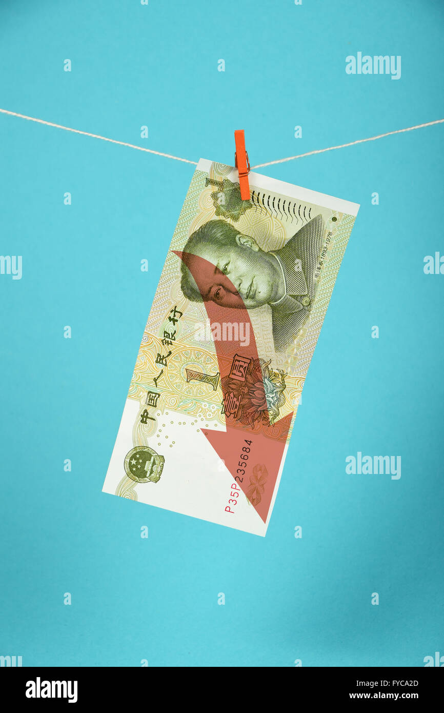 China economy crisis, decline of Chinese yuan, one yuan banknote with red arrow down hanged descending with pin at rope over blu Stock Photo