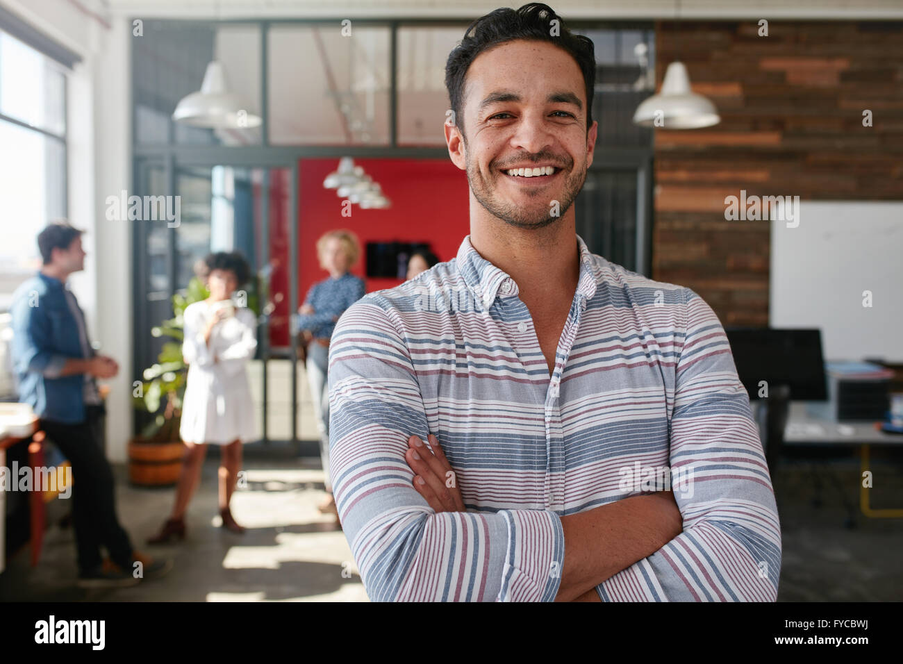 Portrait of a handsome young business man standing with arms crossed in an office. Smart caucasian young male designer with his Stock Photo
