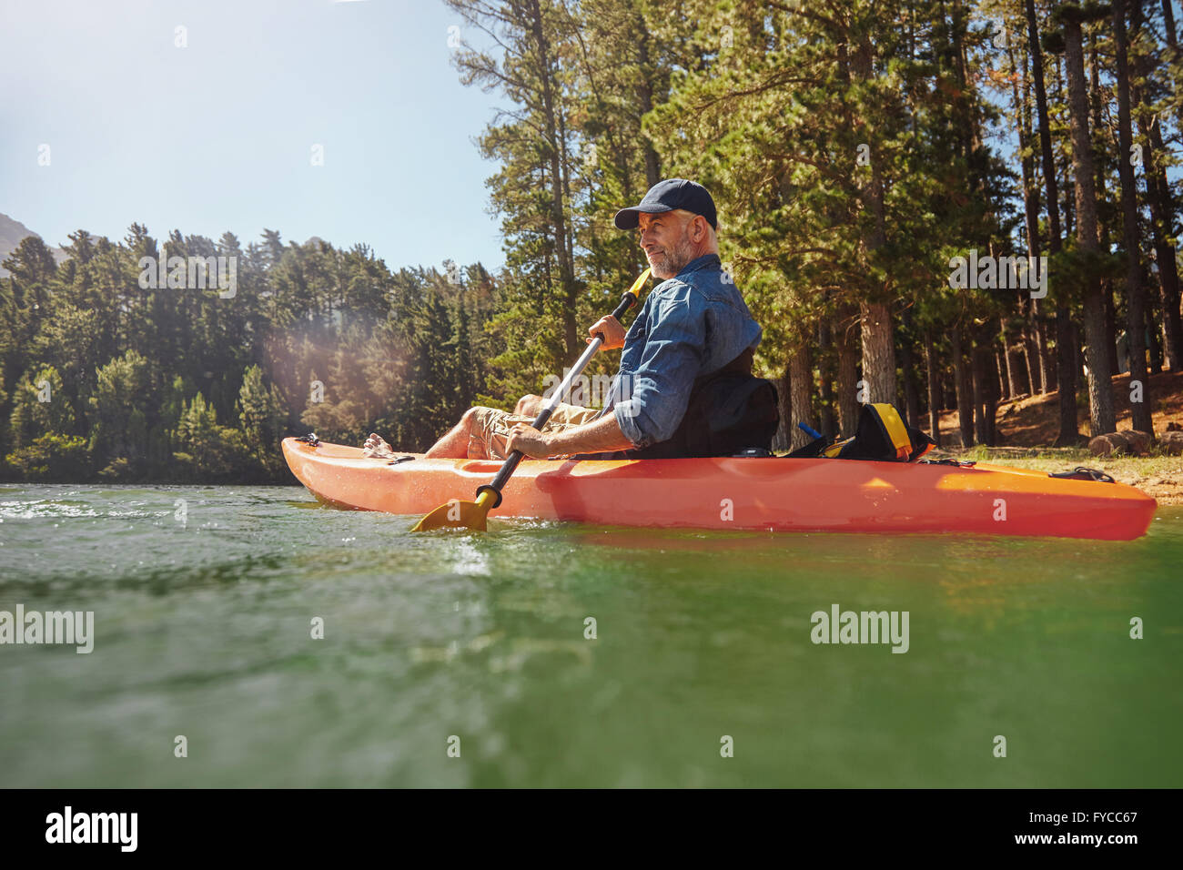 Portrait of a mature man with kayak in a lake. Senior man paddling kayak on a summer day. Stock Photo