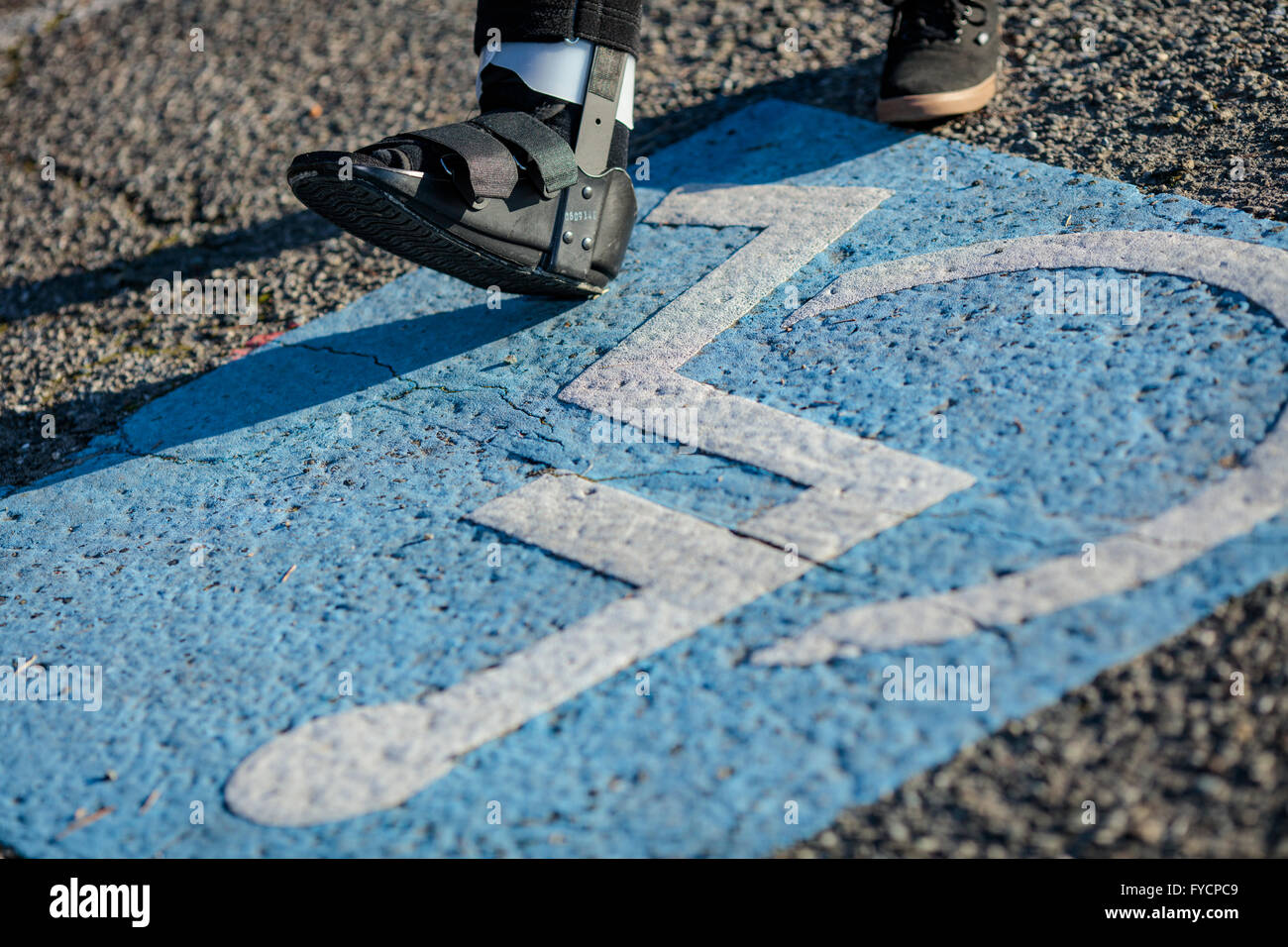 Person with a broken ankle boot steps into a handicapped symbol on a parking spot. Stock Photo