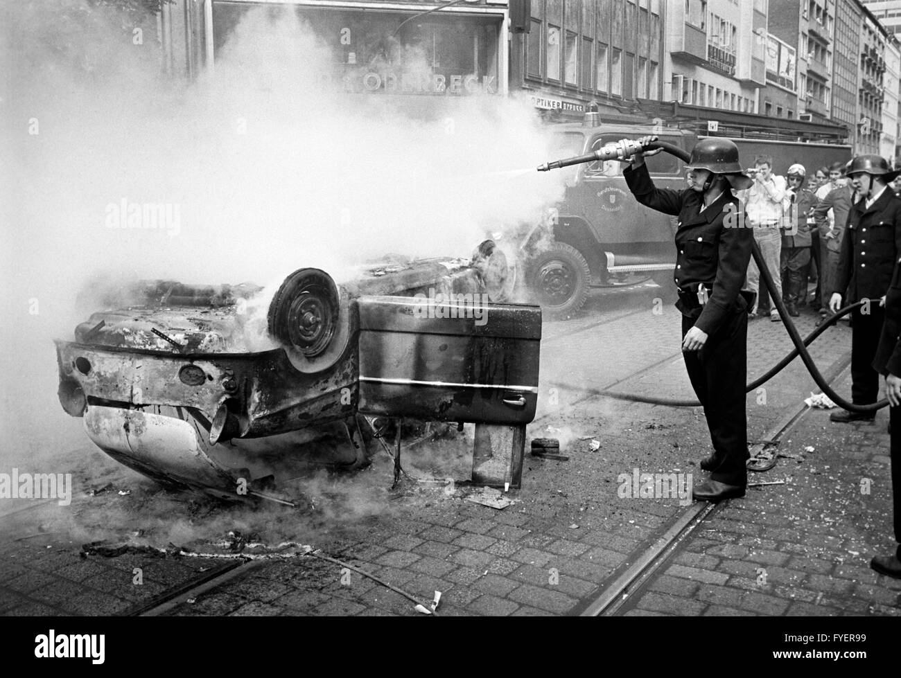 Fireworkers extinguish a burning car in Duesseldorf during a student demonstration on 12 June 1968. Students had brought an old, not functional car to burn. Stock Photo