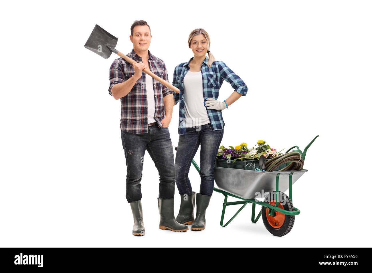 Full length portrait of a woman holding a rake and posing next to a wheelbarrow full of gardening equipment and flowers Stock Photo