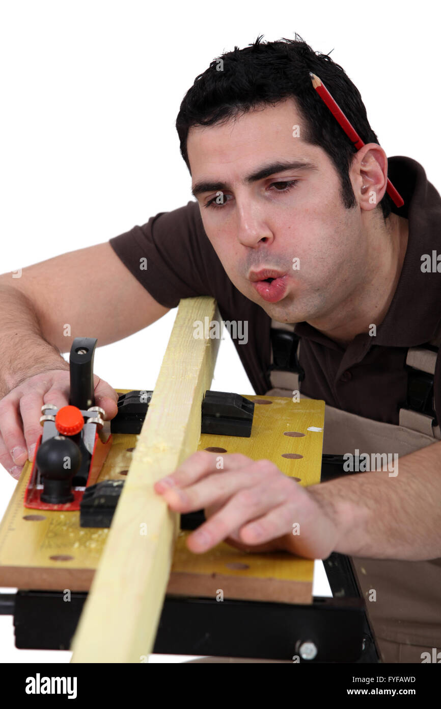 Tradesman blowing shavings off of a wooden plank Stock Photo