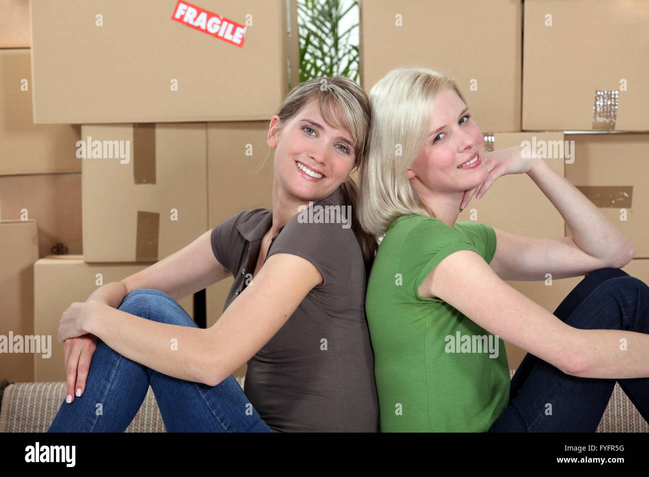 twosome of young girls moving in together sitting back-to-back Stock Photo