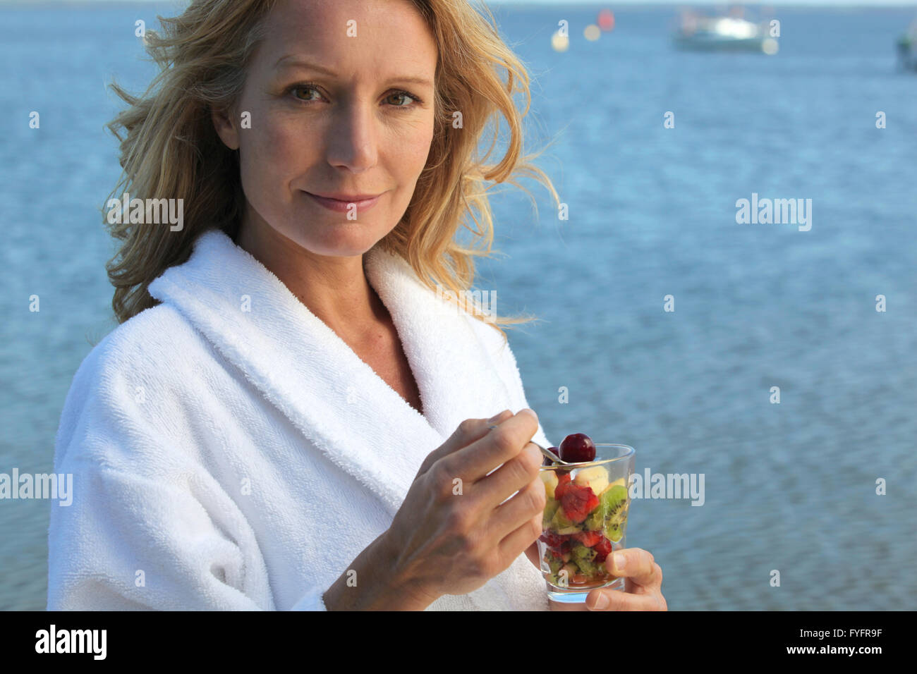 Smiling woman in toweling robe eating fruit salad Stock Photo