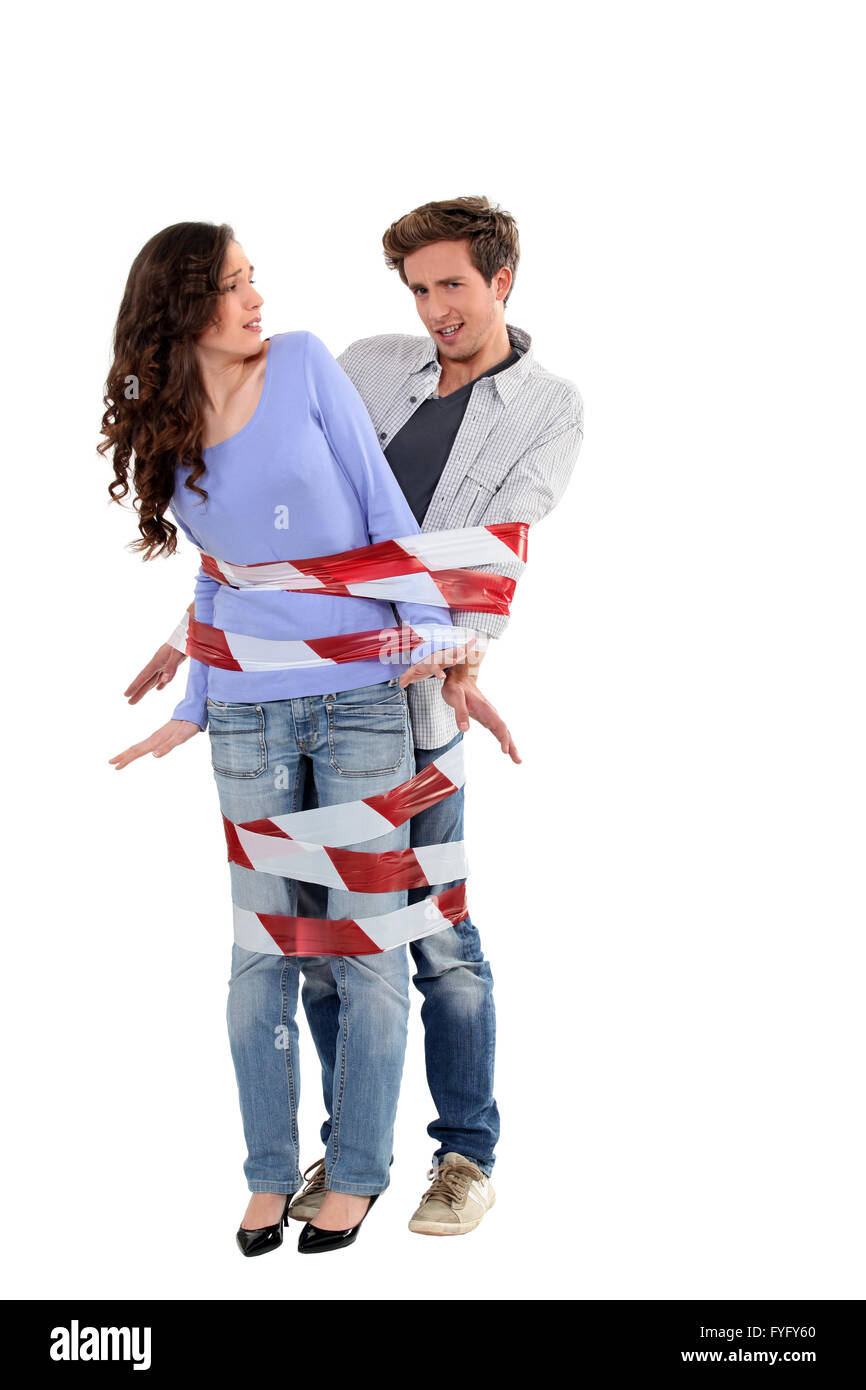 Couple being forcibly held together by caution tape Stock Photo