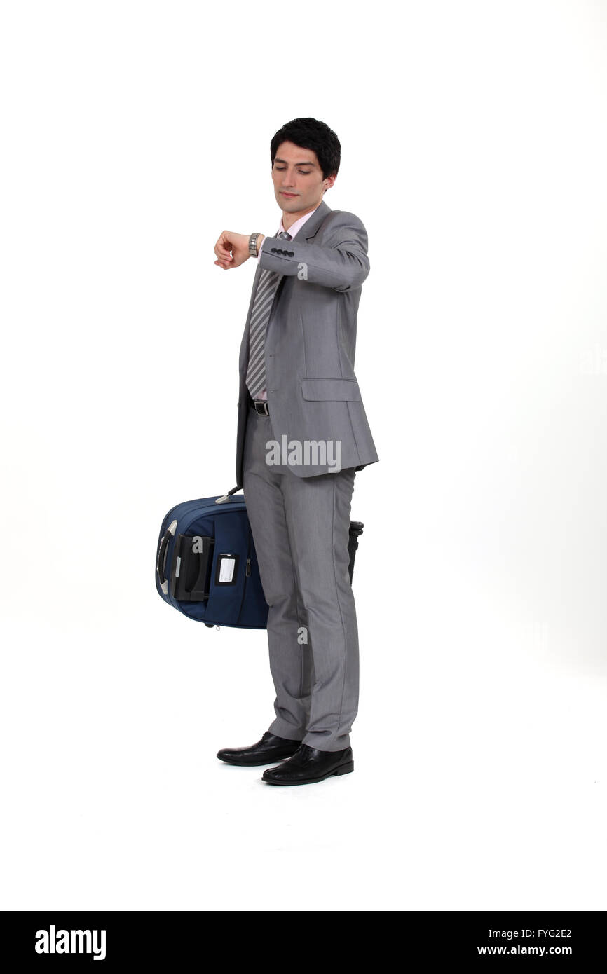 Businessman with suitcase looking at wrist watch Stock Photo
